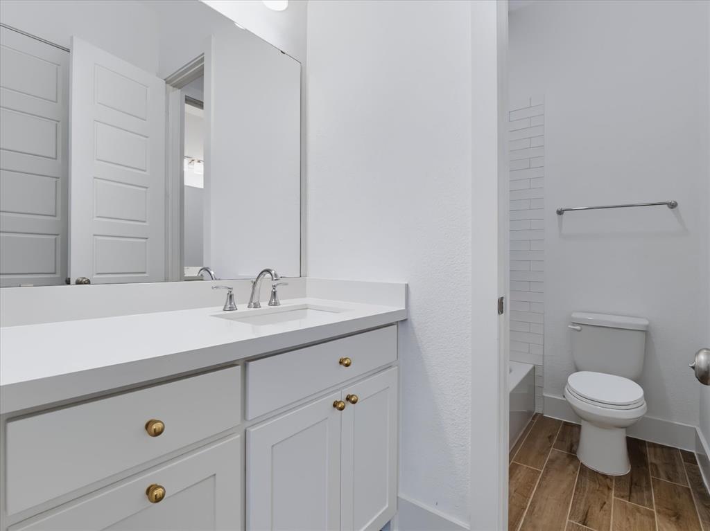 White vanity cabinet with brass-tone hardware, white countertop with integrated sink, polished chrome faucet, wood-finish flooring, and white subway tile wall accents