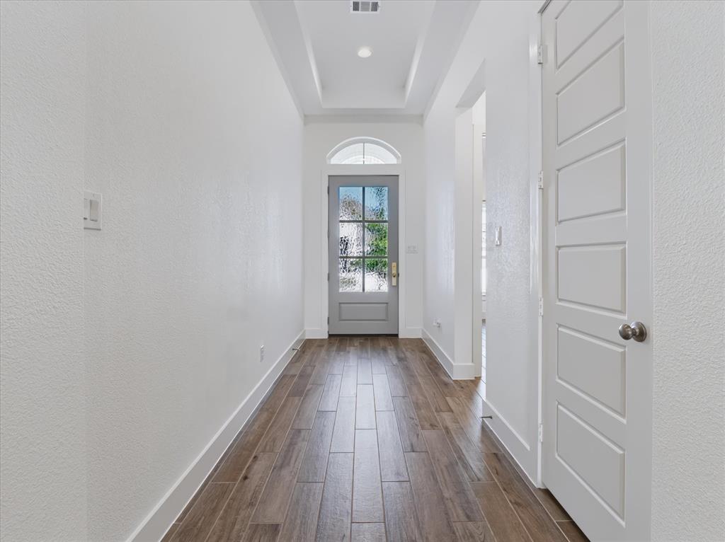 Entryway featuring wood-finish flooring, a tray ceiling, and a six-panel door with a glass-paned upper arch