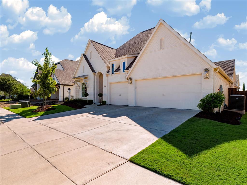 Light-colored brick exterior featuring a multi-gabled roofline, three-car garage, and concrete driveway