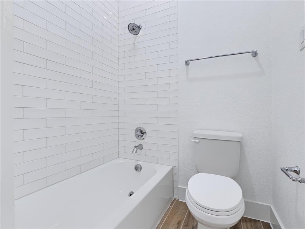 Full-height white subway tile surround, integrated bathtub with polished chrome fixtures, elongated toilet, and wood-finish flooring