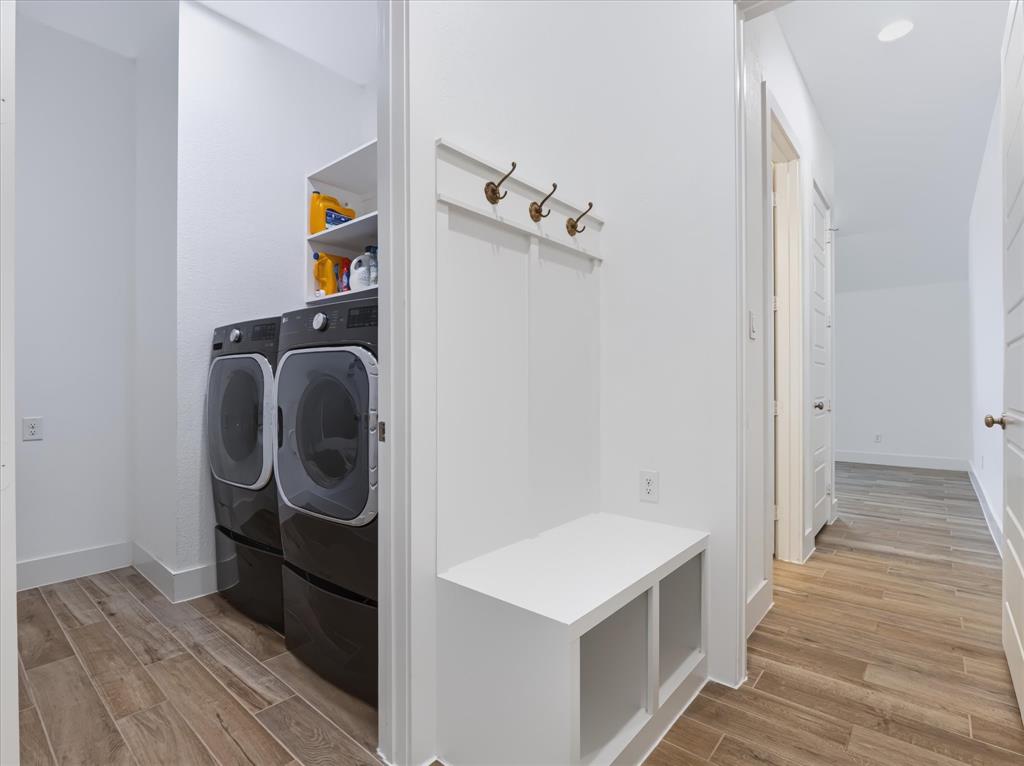 Built-in mudroom bench featuring integrated storage cubbies and a multi-hook coat rack, complemented by wood-finish tile flooring and an enclosed laundry area with recessed shelving