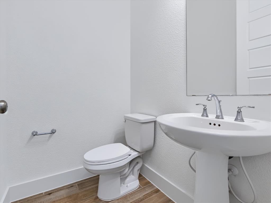 Pedestal sink with a widespread chrome faucet, wall-mounted mirror, white ceramic toilet, and wood-finish flooring