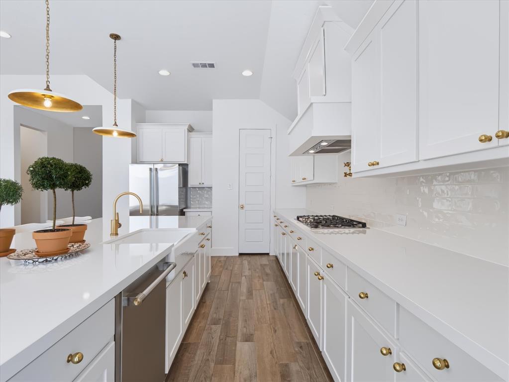 Kitchen featuring white cabinetry, solid surface countertops, a farmhouse-style apron sink, brass-finish hardware, and wood-finish flooring