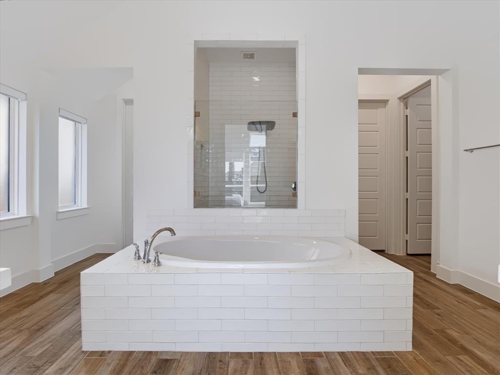 Built-in soaking tub with white subway tile surround, wood-finish flooring, glass-enclosed shower, and polished chrome fixtures