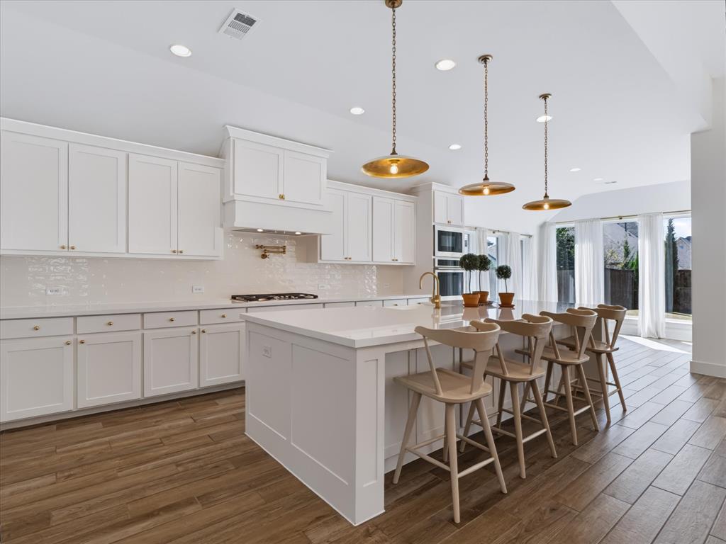 Kitchen featuring white shaker-style cabinetry, a quartz-topped center island with seating, built-in double wall ovens, wood-finish flooring, and metallic pendant lighting