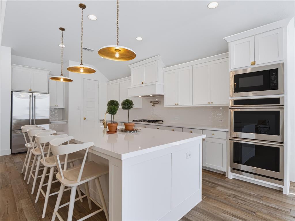 Kitchen featuring white cabinetry, quartz countertops, wood-finish flooring, stainless steel built-in double wall ovens, and pendant lighting
