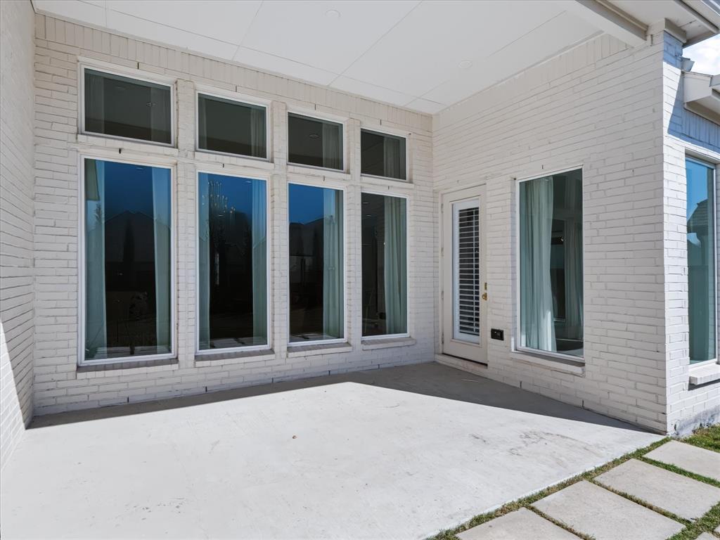 Covered patio featuring white brick exterior walls, concrete flooring, large floor-to-ceiling windows, and glass-paneled exterior door