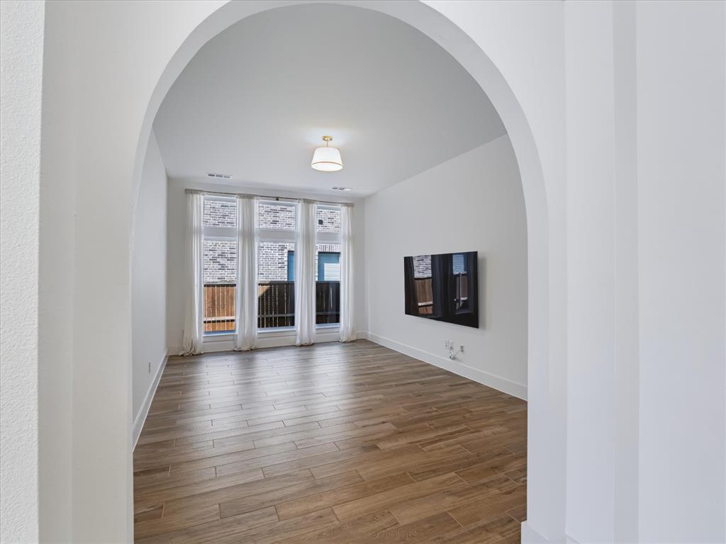 Interior space featuring an architectural arched entryway, wood-finish flooring, a wall-mounted light fixture, and floor-to-ceiling windows
