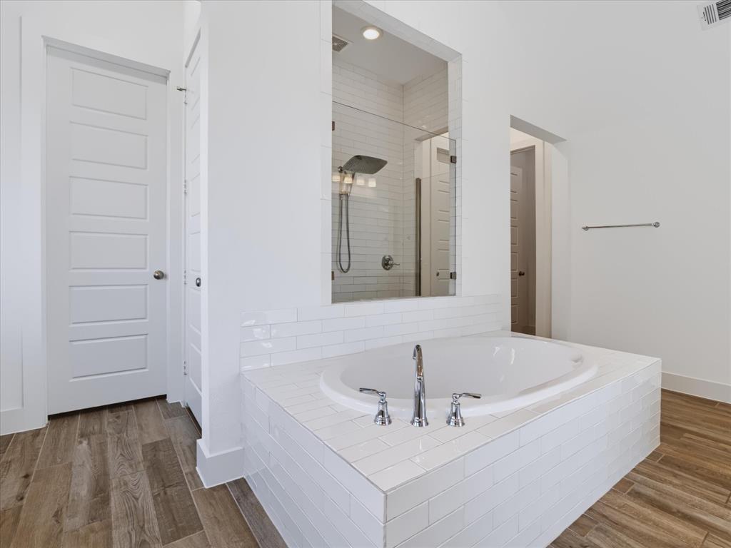 Oval soaking tub with polished chrome fixtures, white subway tile surround, recessed glass-enclosed shower, and wood-finish flooring