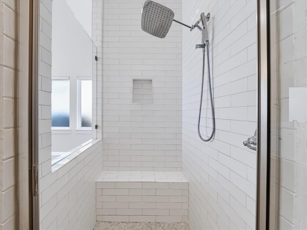 Walk-in shower featuring white subway tile walls, a built-in bench, a recessed wall niche, a square rainfall showerhead, and a hand-held sprayer