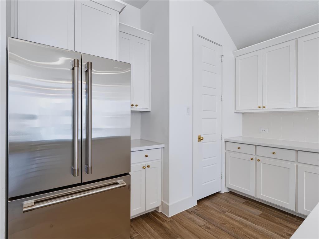 Kitchen area featuring white shaker-style cabinetry, stainless steel French door refrigerator, solid-surface countertops, and wood-finish flooring