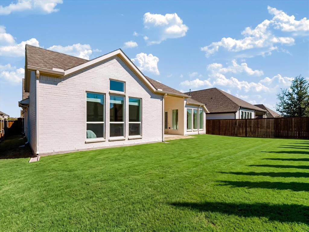 Light-colored brick exterior featuring oversized windows, a pitched shingle roof, and a fenced backyard with a lawn