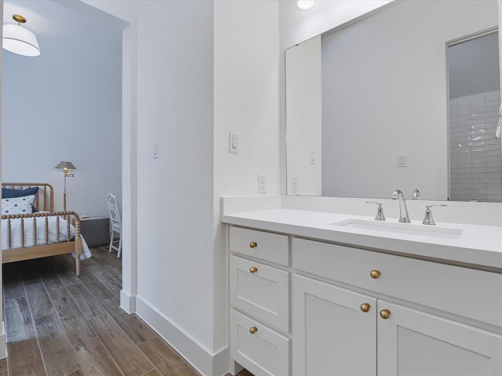 Bathroom vanity featuring white cabinetry, a solid-surface countertop, an integrated rectangular sink, brass-finish hardware, and a large-format vanity mirror