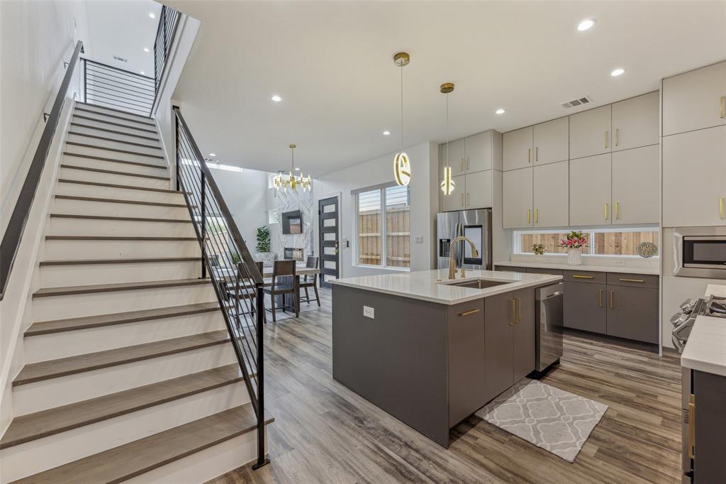 Kitchen with stainless steel appliances, sink, a kitchen island with sink, pendant lighting, and wood-type flooring