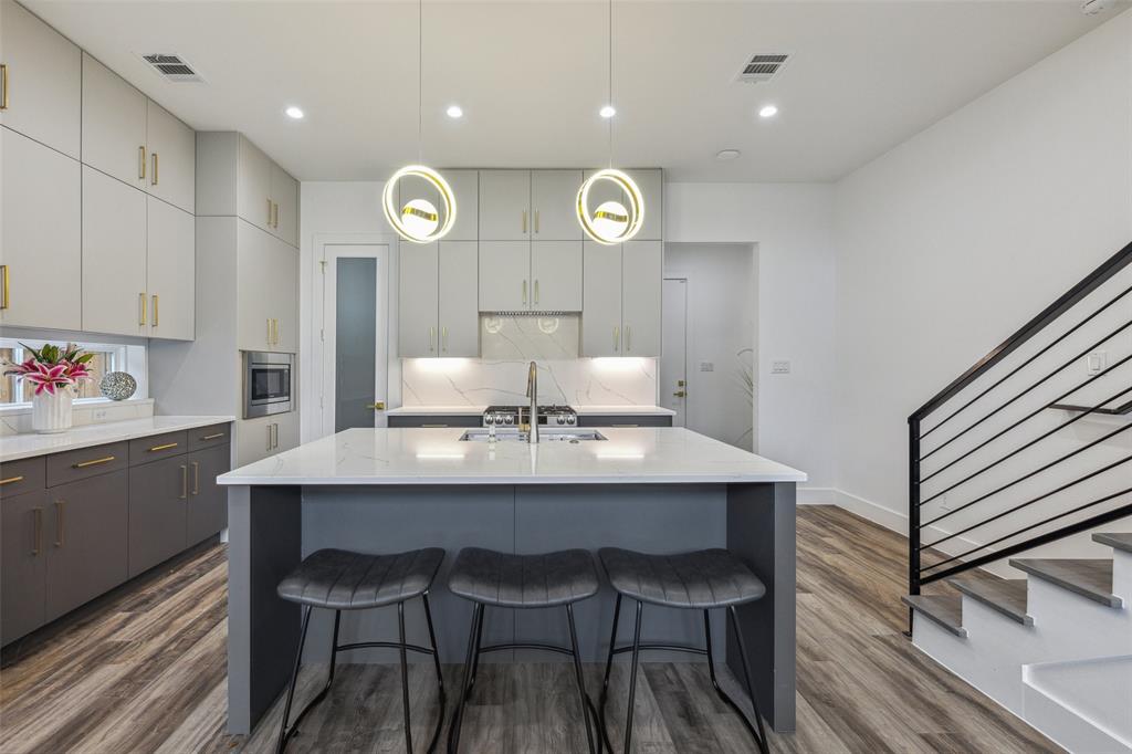 Kitchen featuring backsplash, hanging light fixtures, stainless steel microwave, hardwood / wood-style flooring, and a center island with sink