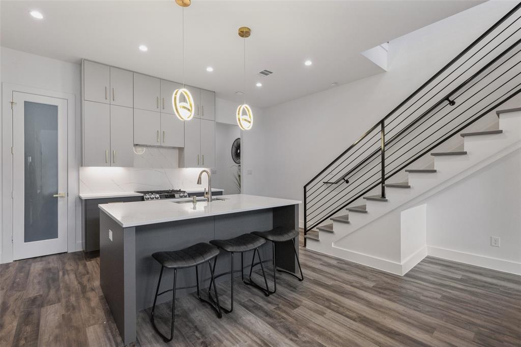 Kitchen with sink, gray cabinetry, a kitchen island with sink, dark hardwood / wood-style flooring, and hanging light fixtures