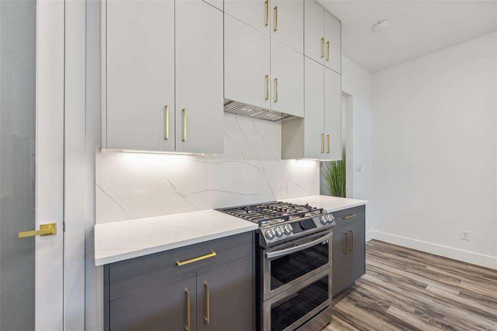 Kitchen featuring light wood-type flooring, tasteful backsplash, double oven range, white cabinetry, and light stone countertops