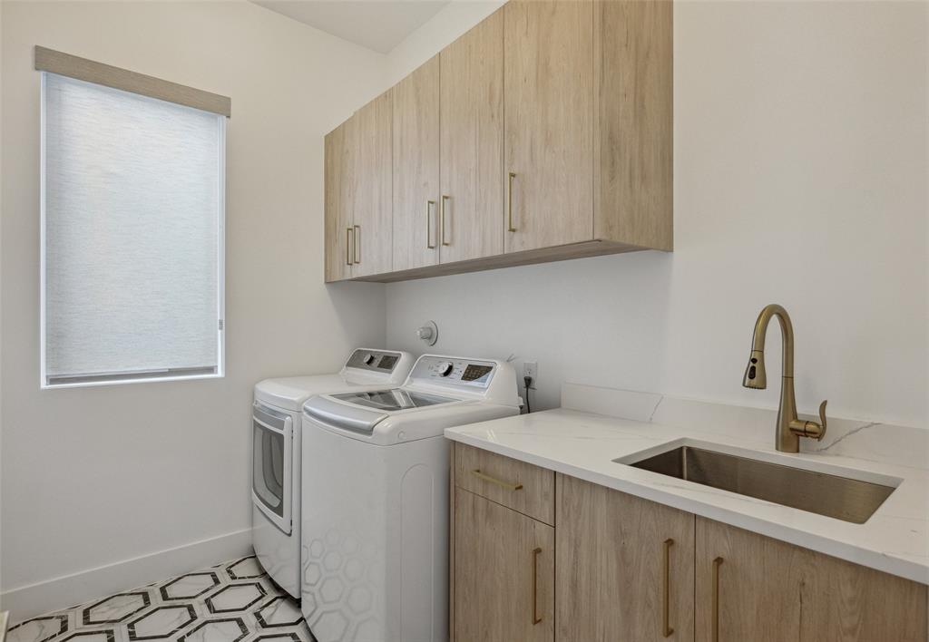 Laundry room with light tile patterned floors, sink, washing machine and clothes dryer, and cabinets