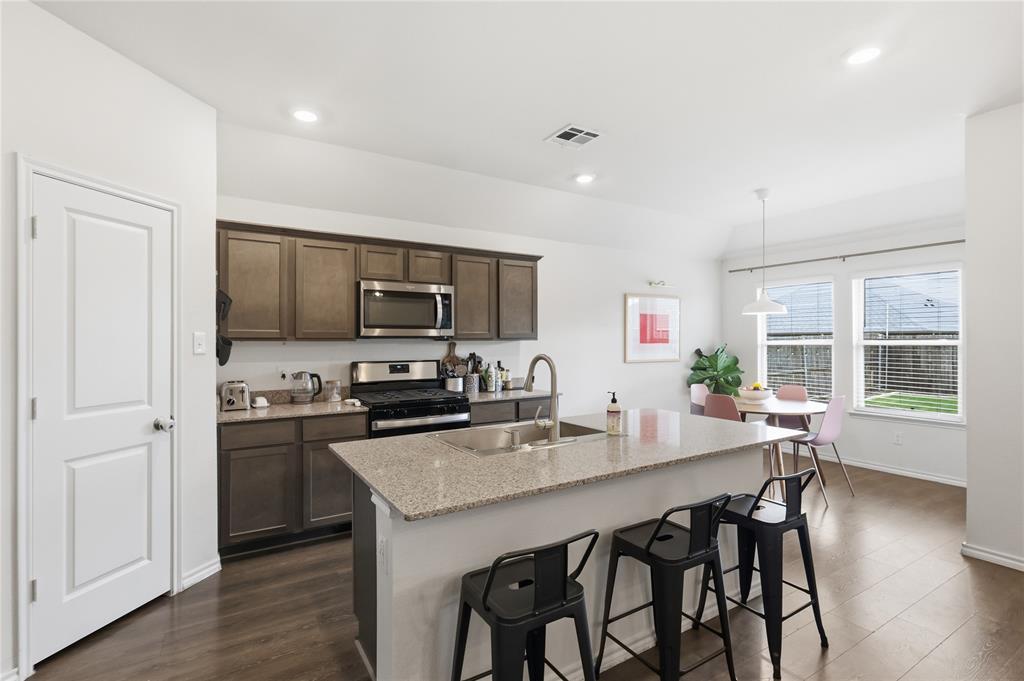 Kitchen featuring dark-toned cabinetry, a spacious island with stone-finish countertops, stainless steel appliances, wood-finish flooring, and recessed lighting