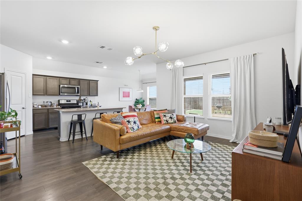 Open-concept living space featuring wood-finish flooring, a kitchen with dark cabinetry and a central island, recessed lighting, and a multi-globe chandelier