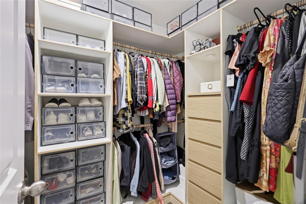 Custom walk-in closet featuring white laminate shelving, stacked cubbies, tiered hanging rods, and a built-in chest of drawers with light-toned wood-finish fronts
