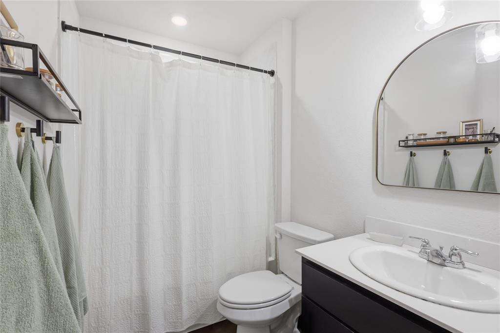 Bathroom featuring a vanity with a white countertop and oval under-mount sink, an arched wall-mounted mirror, matte black hardware, and a built-in wall shelf
