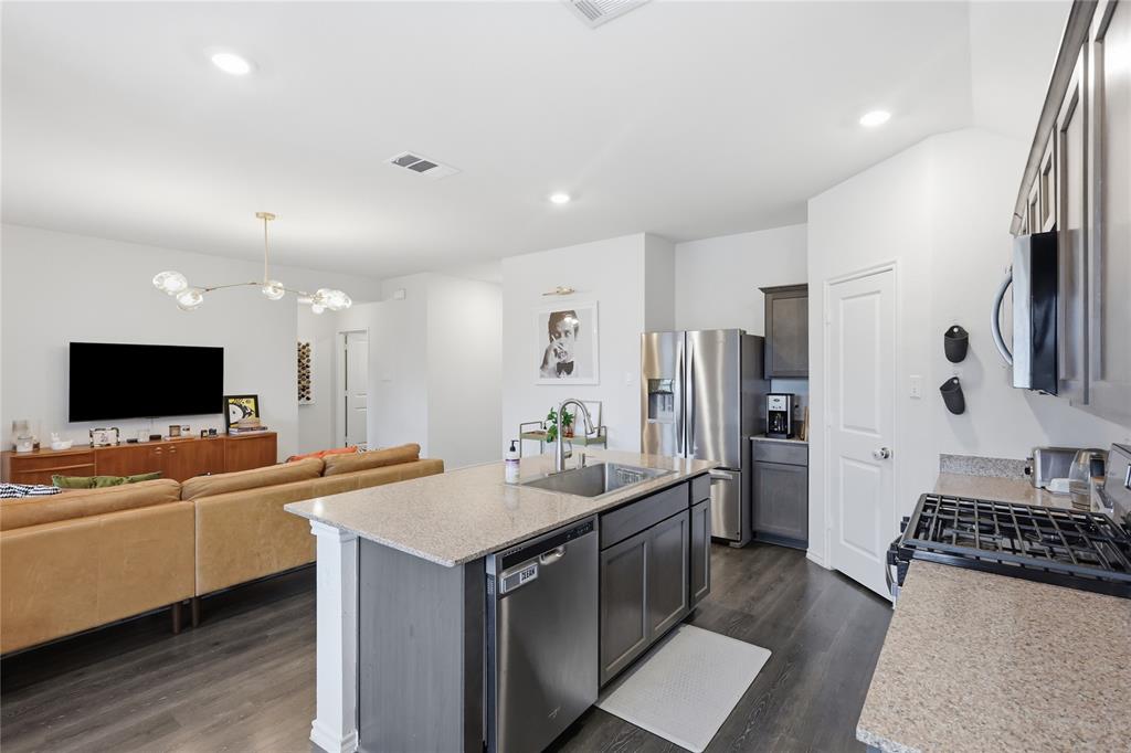 Kitchen featuring a central island with stone-surface countertops, dark wood cabinetry, recessed lighting, and stainless steel appliances, complemented by wood-finish flooring