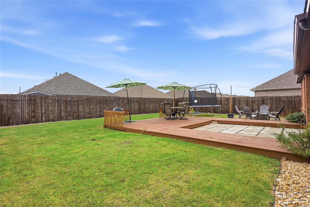 Rear yard featuring a wood deck with an integrated stone paver patio, a perimeter wood privacy fence, and an expansive lawn
