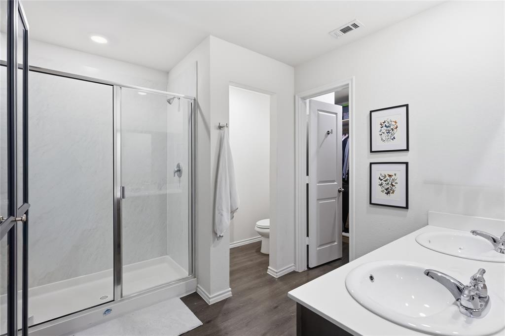 Bathroom featuring a dual-sink vanity with a solid-surface countertop, walk-in shower with a glass enclosure, wood-finish flooring, and recessed lighting