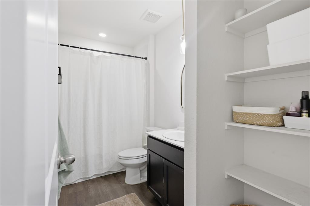 Bathroom featuring wood-finish flooring, a dark-toned vanity with a white countertop, recessed lighting, and built-in wall shelving