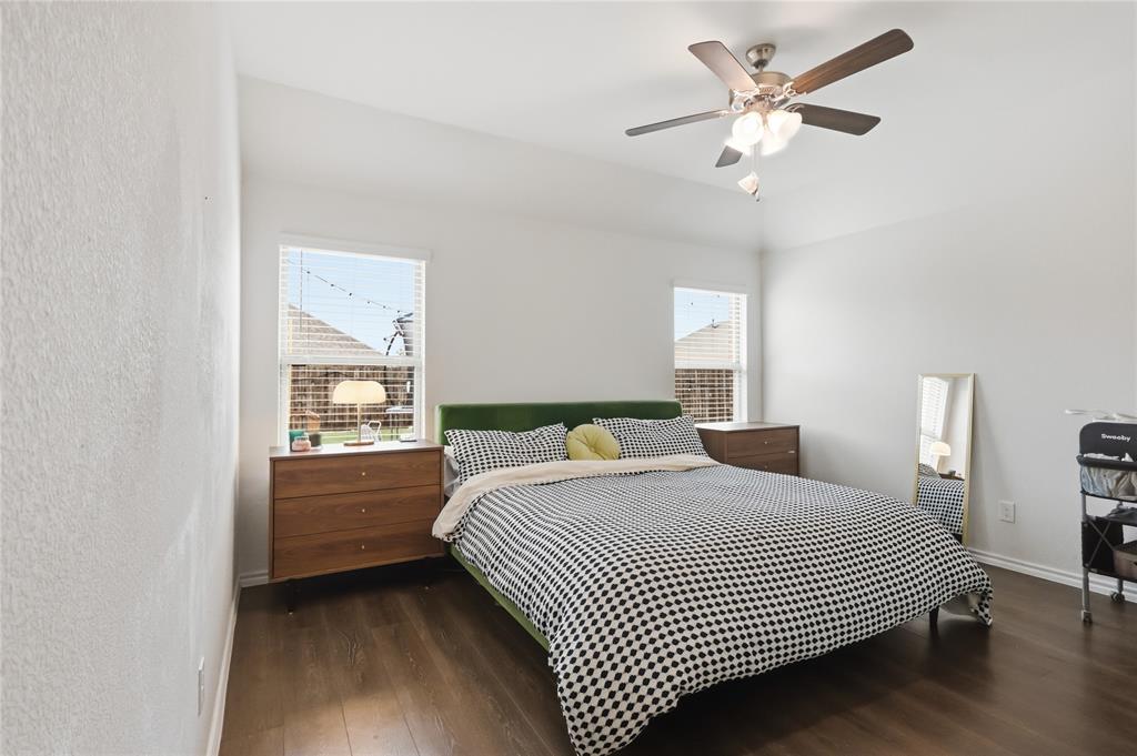 Room featuring wood-finish flooring, high tray ceilings, two windows, and a multi-blade ceiling fan with integrated light fixture