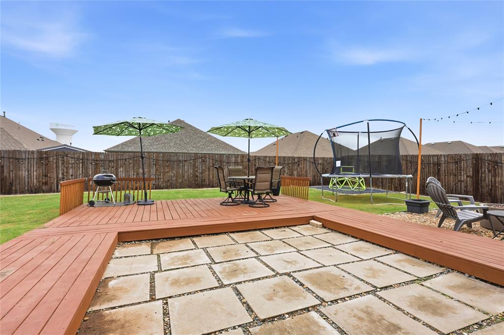 Backyard featuring a raised wood-finish deck, a rectangular stone paver patio area, and a wood privacy fence