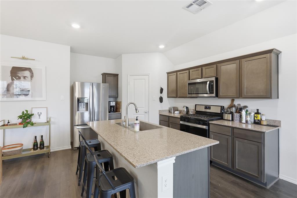 Kitchen featuring shaker-style cabinetry, stone-surface countertops, a center island with an undermount sink, stainless steel appliances, and wood-finish flooring