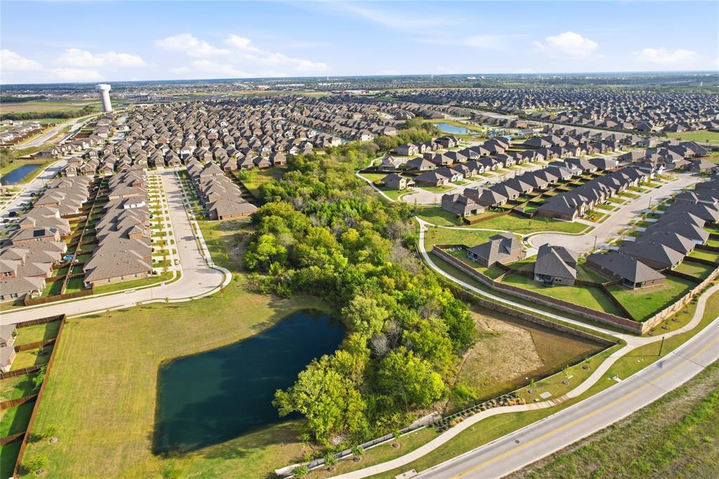 Aerial perspective of a master-planned community featuring a central pond, established tree canopy, paved sidewalk infrastructure, and street lighting
