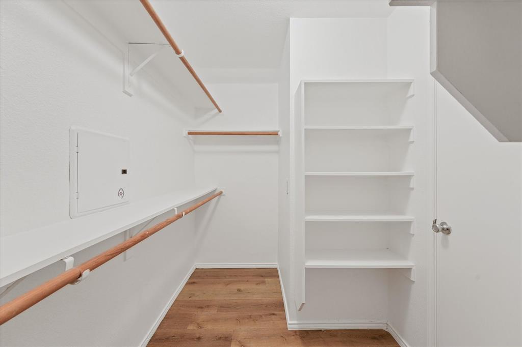 Storage space featuring wood-finish flooring, white built-in shelving, and wood-toned hanging rods
