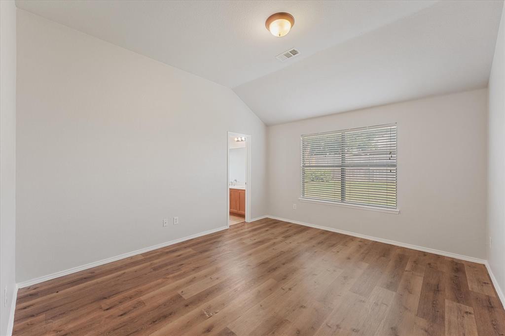 Vaulted ceiling with neutral wall tones, wood-finish flooring, and a single-pane window with integrated horizontal blinds