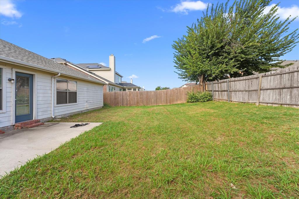 Backyard featuring a concrete patio, wood privacy fencing, and a mature tree