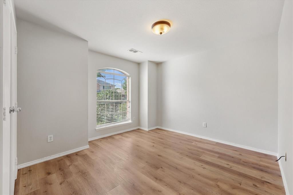 Neutral-toned interior featuring wood-finish flooring, an arched window, and a flush-mount ceiling light Neutral-toned interior featuring wood-finish flooring, an arched window, and a flush-mount ceiling light