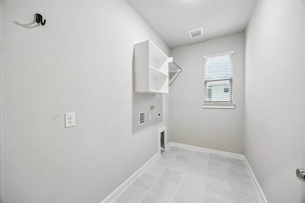 Utility room featuring large-format ceramic tile flooring, built-in shelving, a metal hanging rod, and a single-hung window with horizontal blinds