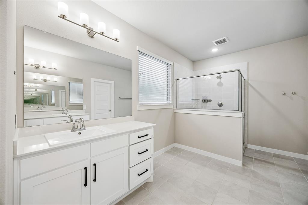 Bathroom featuring a white vanity with drawers, a rectangular undermount sink, a large wall-to-wall mirror, and a glass-enclosed shower with tile surround