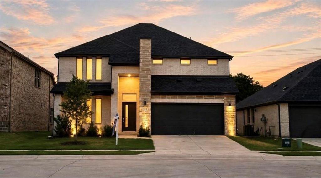 Two-story exterior featuring light-toned brick facade, vertical window accents, stone-clad chimney, dark-toned roof shingles, and an attached multi-car garage