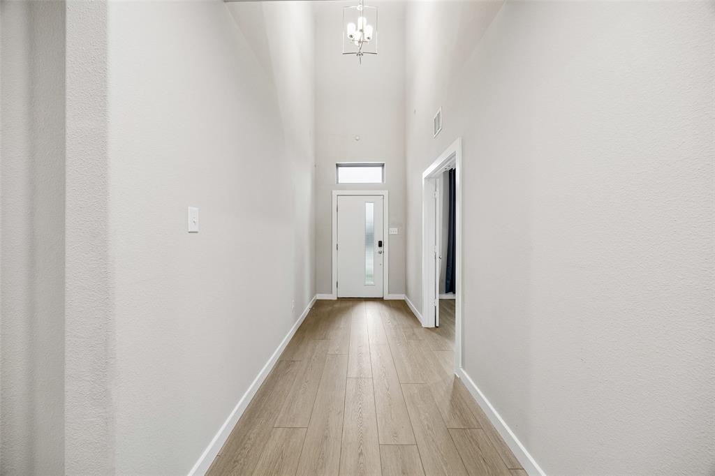 Entryway featuring high ceilings, wood-finish flooring, a metal pendant light fixture, and a glass-paneled entry door with a transom window