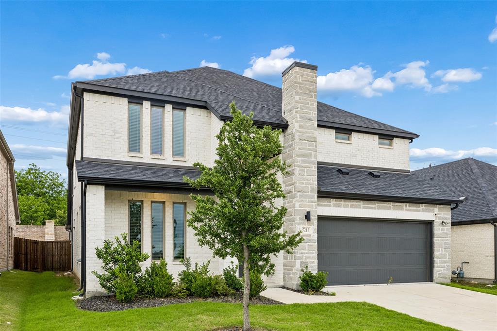 Two-story exterior featuring a white brick and stone facade, a multi-gabled asphalt shingle roof, a two-car garage with a paneled door, and a covered entryway