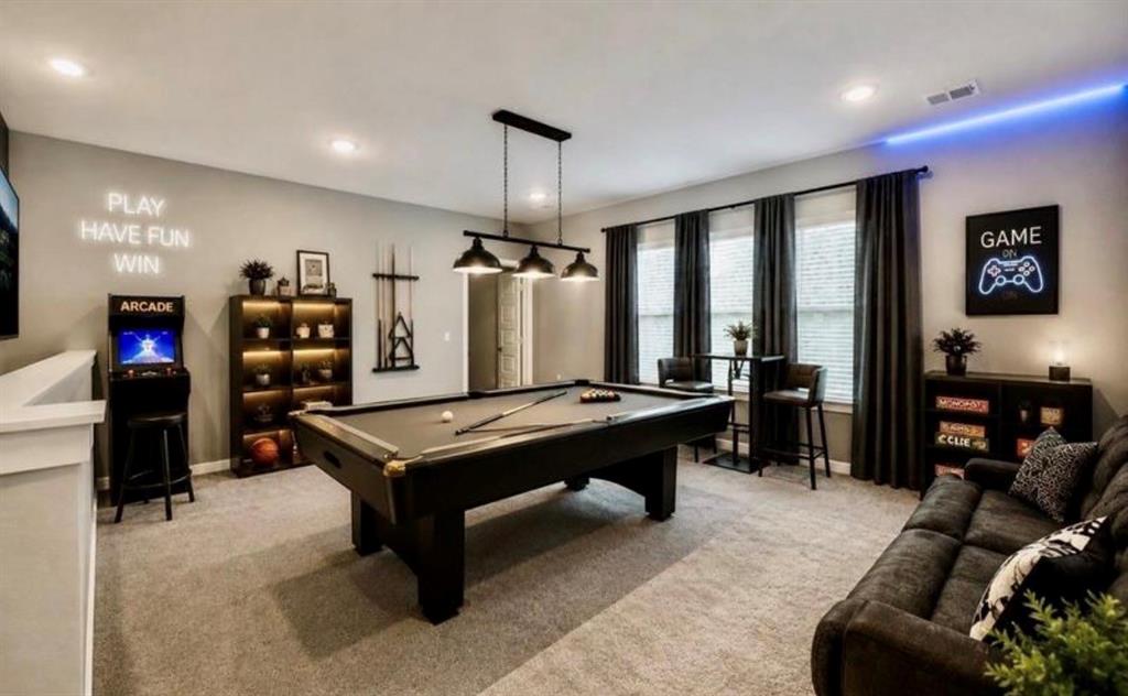Spacious room featuring neutral carpeting, recessed ceiling lighting, a three-bulb industrial pendant light, and triple windows with full-height drapery
