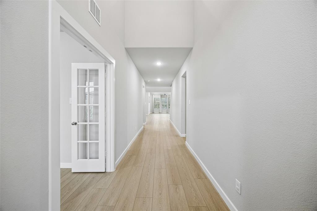 Hallway featuring high ceilings, wood-finish flooring, recessed lighting, and a white French door