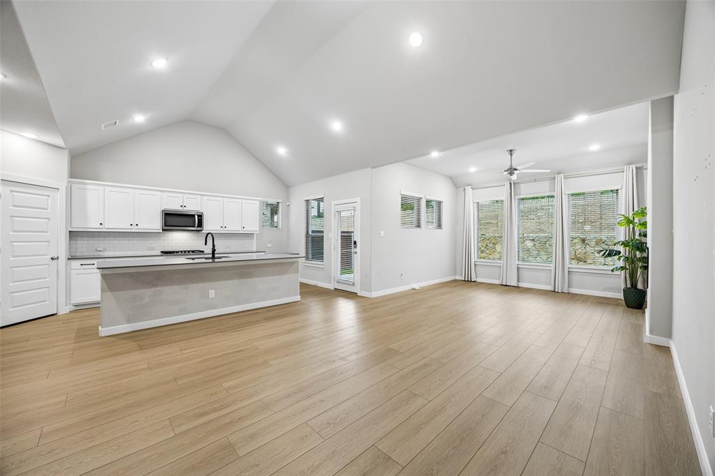 Vaulted ceilings, wood-finish flooring, recessed lighting, kitchen island with a matte black faucet, and large windows with integrated trim