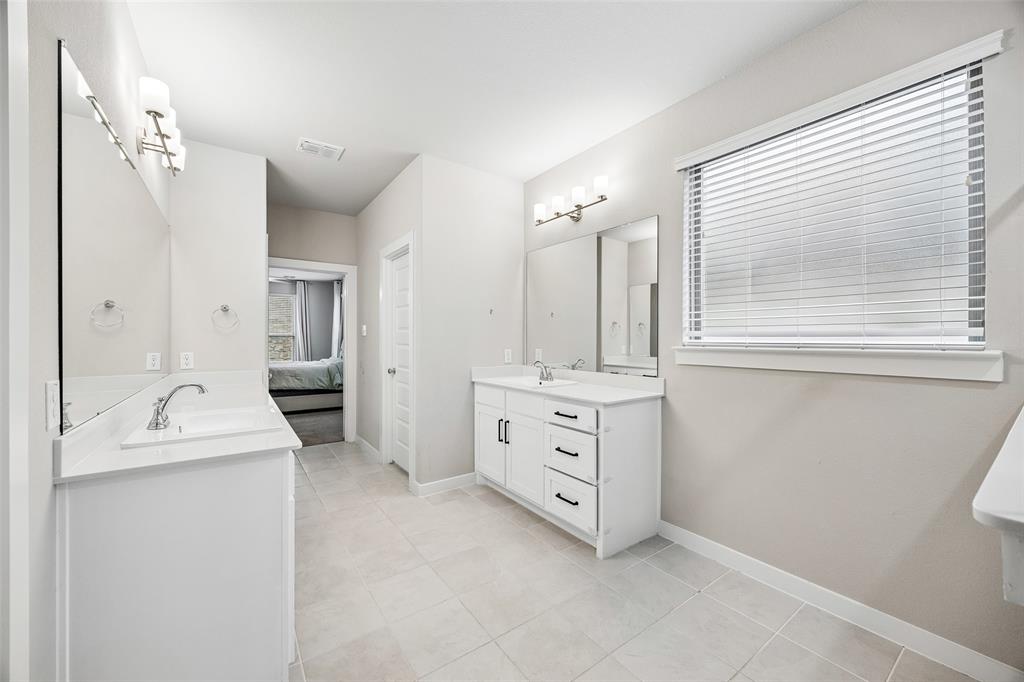 Dual vanity area featuring white cabinetry with dark hardware, stone-style countertops, large rectangular wall mirrors, polished chrome fixtures, and ceramic tile flooring