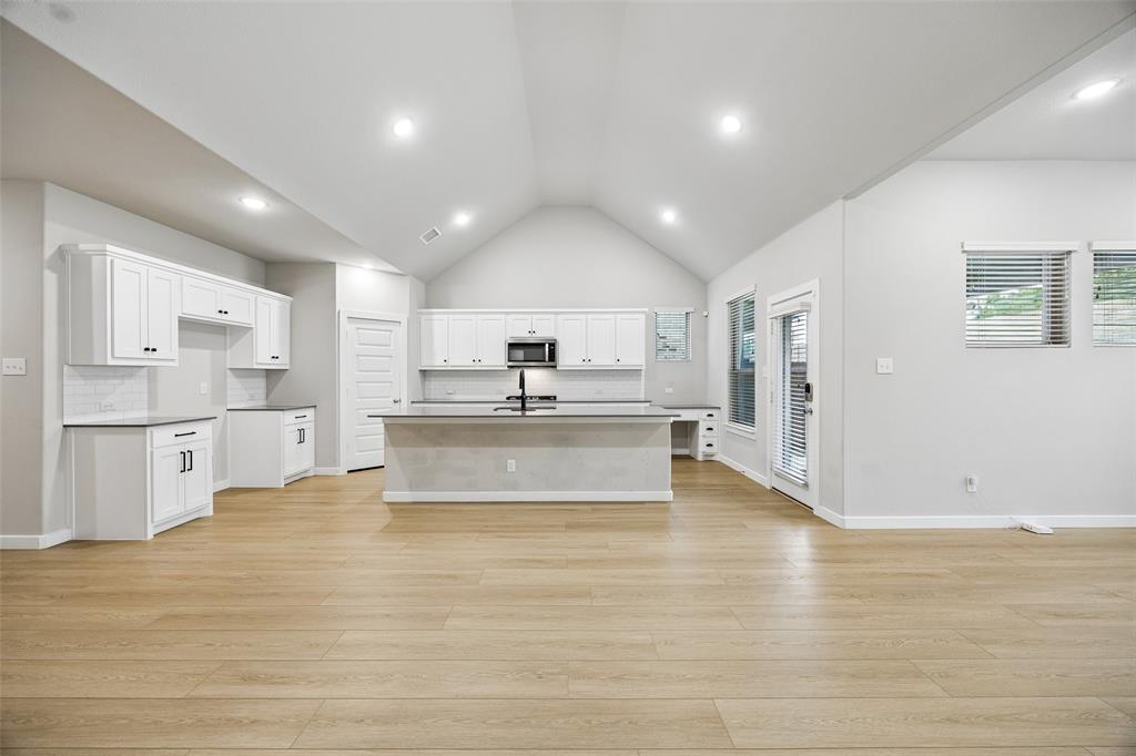 Vaulted ceilings, wood-finish flooring, white cabinetry, a center island, and recessed lighting
