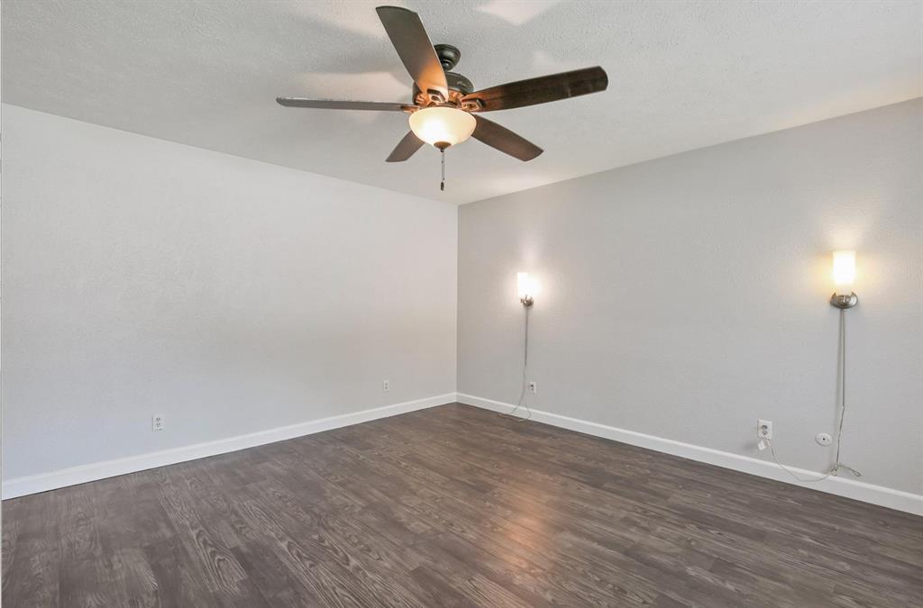 Room featuring wood-finish flooring, a central ceiling fan with integrated lighting, and two wall-mounted light fixtures