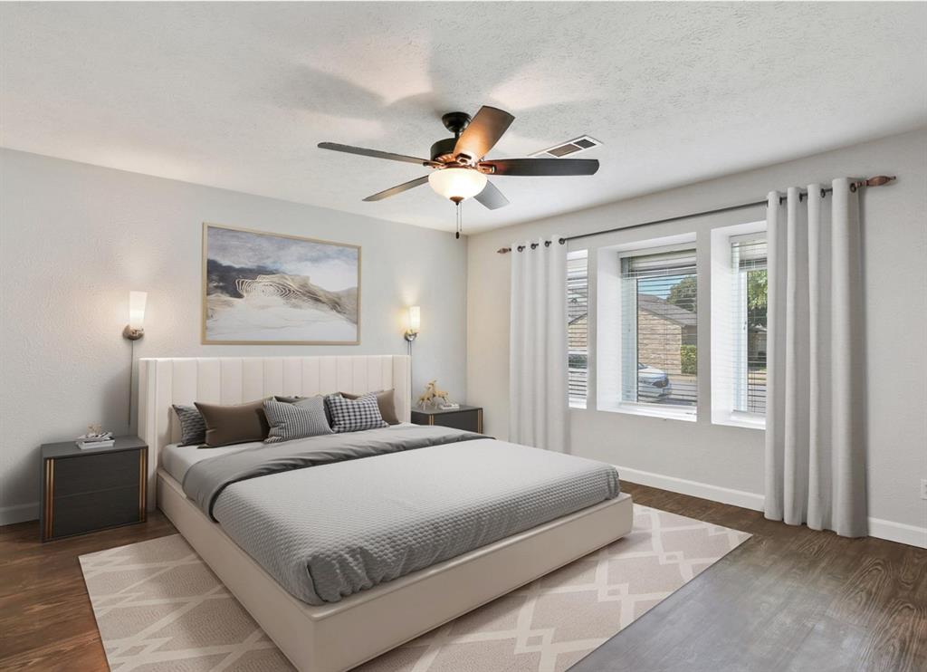 Bedroom featuring wood-finish flooring, three windows with natural light, a ceiling fan with integrated light fixture, and two wall-mounted sconces